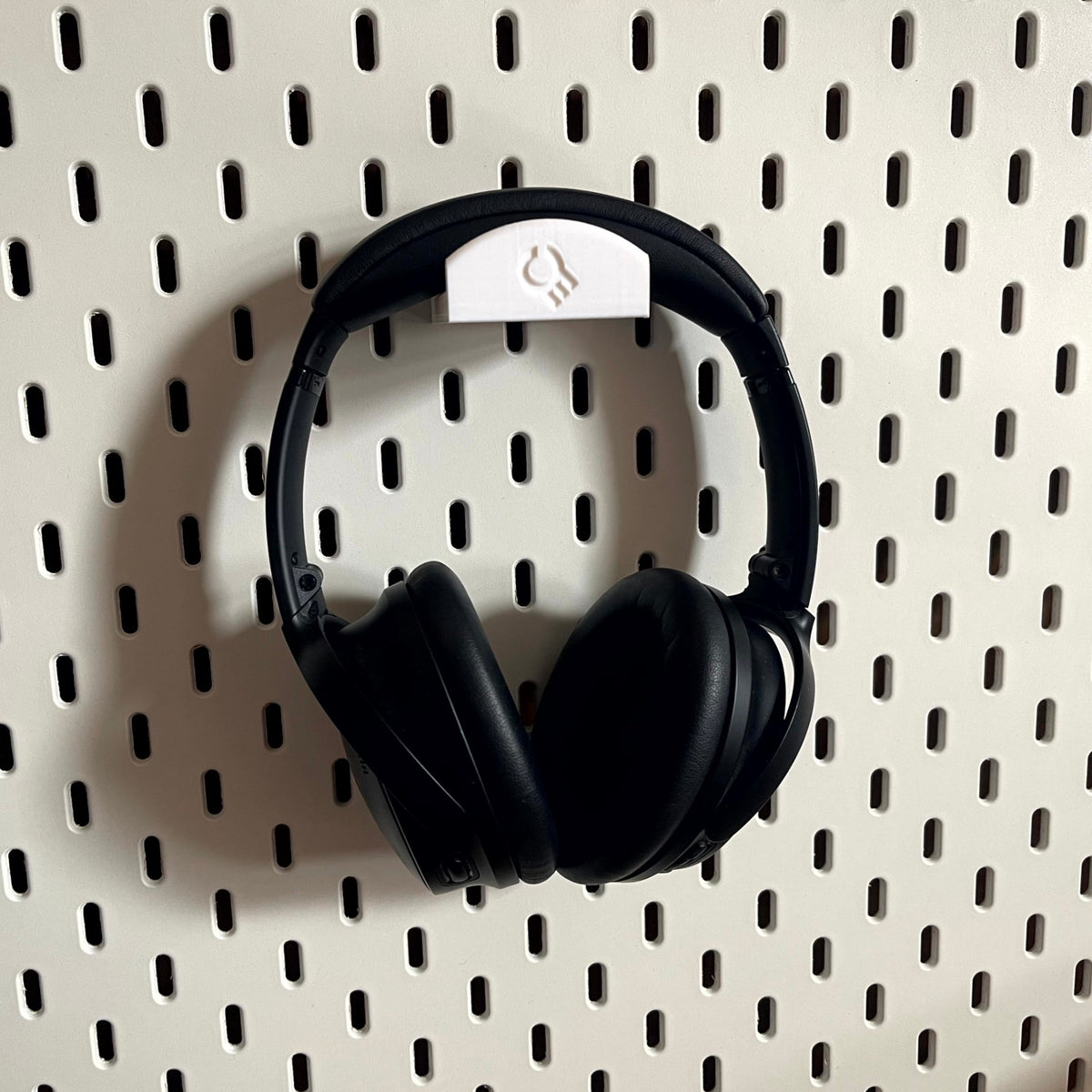 3D printed Headphone Holder for IKEA SKADIS UPPSPEL Headphones by Cold Earth Industries, shown in White, holding black headphones, on a white Ikea Skadis Pegboard– custom studio and live performance gear.