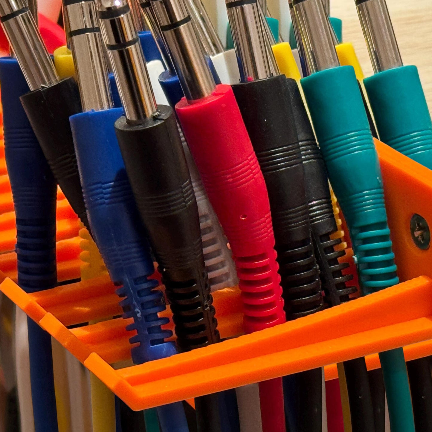 3D printed Guitar Pedal Patch Cable Holder by Cold Earth Industries, shown with cables in orange screwed to the side of a desk – custom studio and live performance gear.