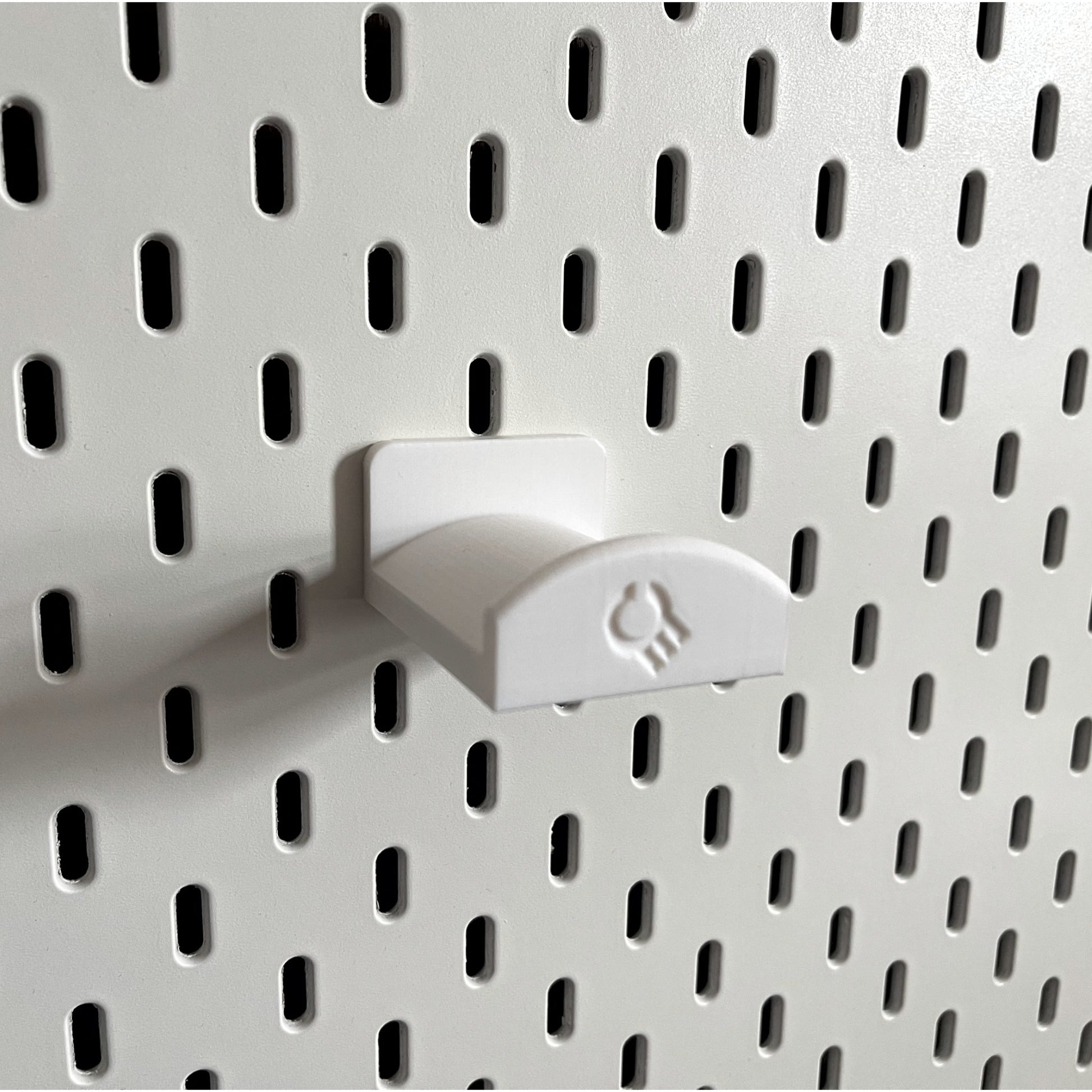 3D printed  Headphone Holder for IKEA SKADIS UPPSPEL Headphones by Cold Earth Industries, shown in White, on a white Ikea Skadis Pegboard– custom studio and live performance gear.
